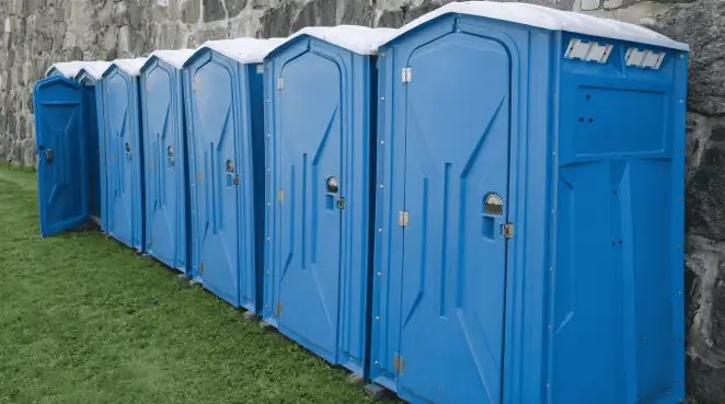 Row of blue portable toilets lined up on grass against a stone wall for event sanitation in Tempe, AZ